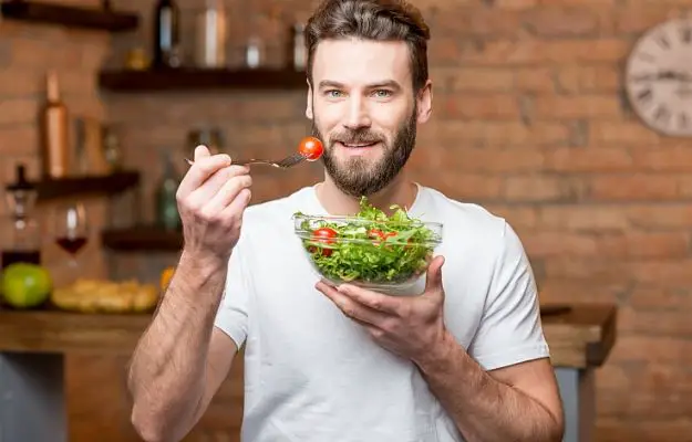 Handsome bearded man in white t-shirt eating salad in the kitchen | eat right | 7 Ways To Invest In Yourself This Year (And Why It Matters)