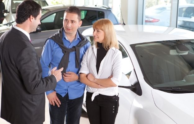 一個汽車推銷員正在跟一對夫婦在後面跟車說話- ca |  談判汽車價格的 5 個技巧  這是一項商業交易