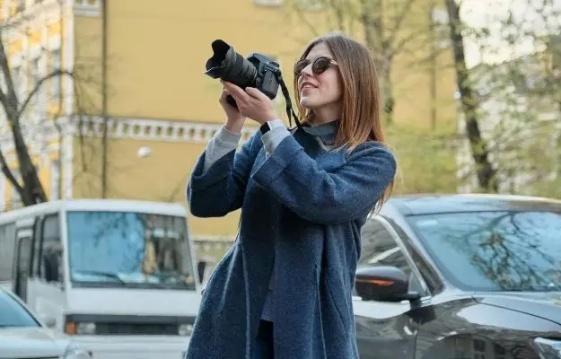 一個女孩穿著外套，拿著相機，後面有2輛車| 高分辨率照片| CLIPARTO  選擇一個主題 |  成為更好的攝影師 I 拍攝更好照片的 9 個技巧